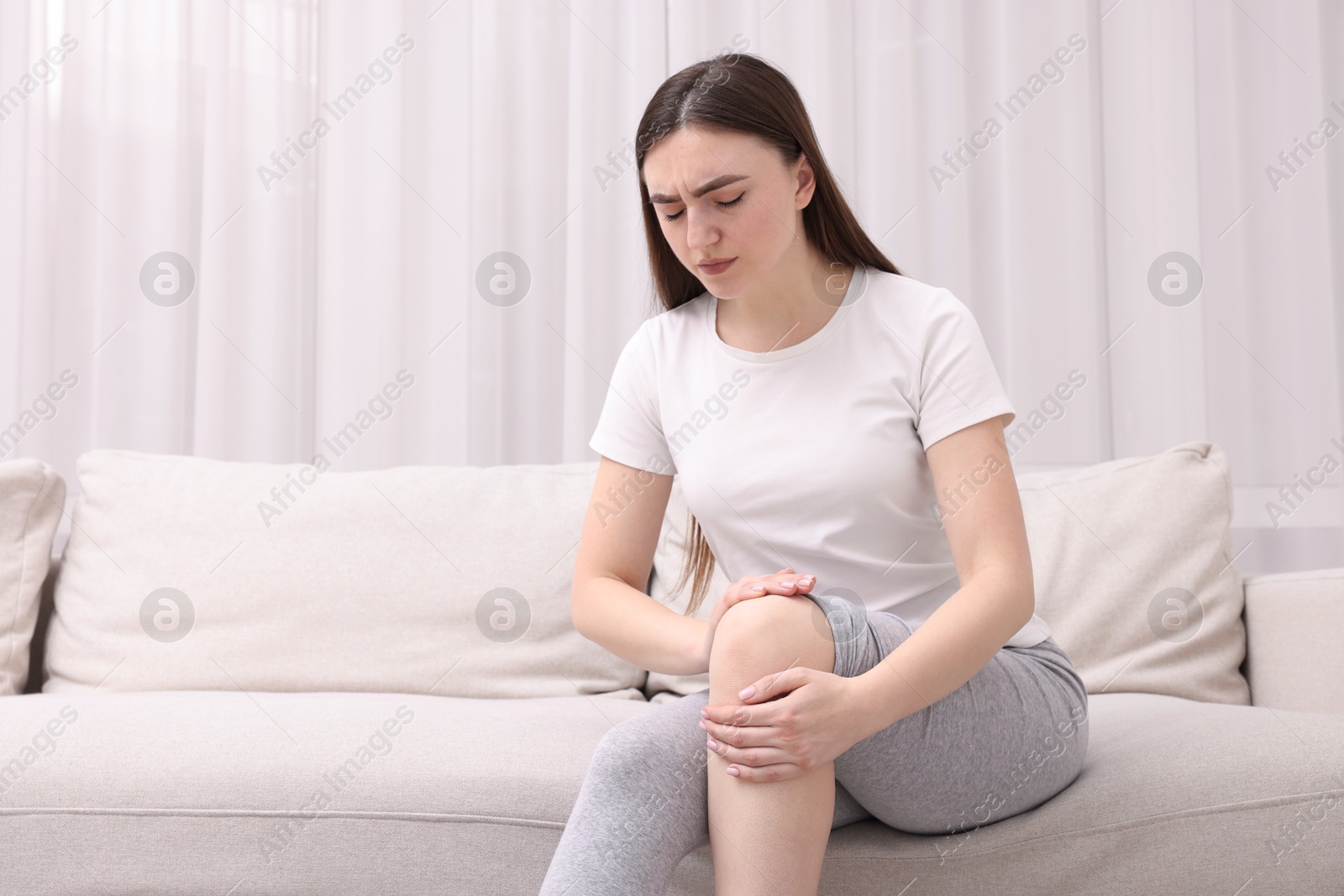 Photo of Young woman suffering from pain in knee on sofa at home. Space for text