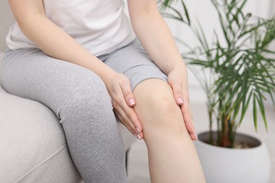 Photo of Young woman suffering from pain in knee on sofa at home, closeup