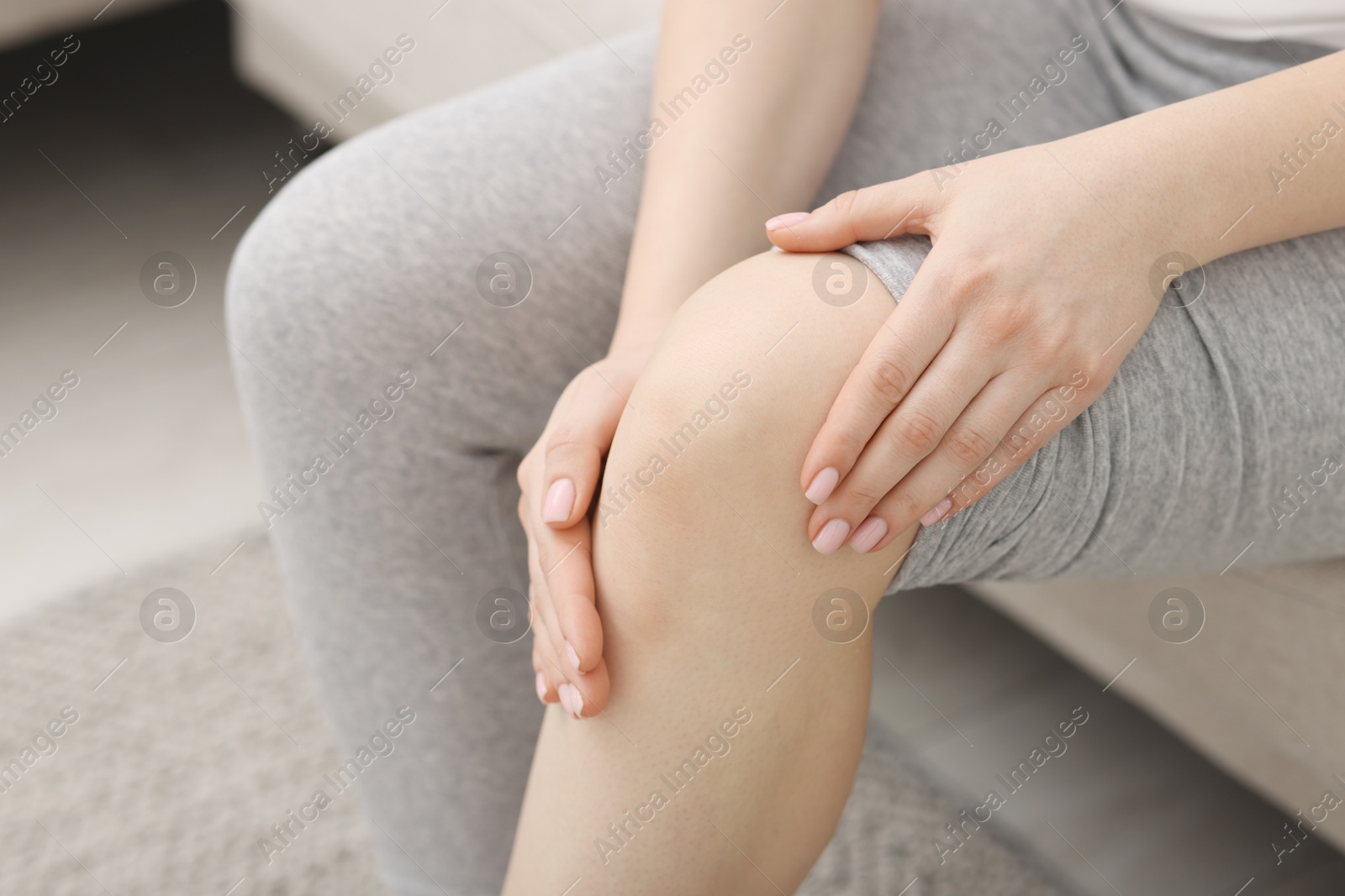 Photo of Young woman suffering from pain in knee on sofa at home, closeup