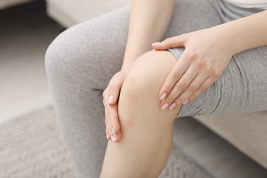 Photo of Young woman suffering from pain in knee on sofa at home, closeup