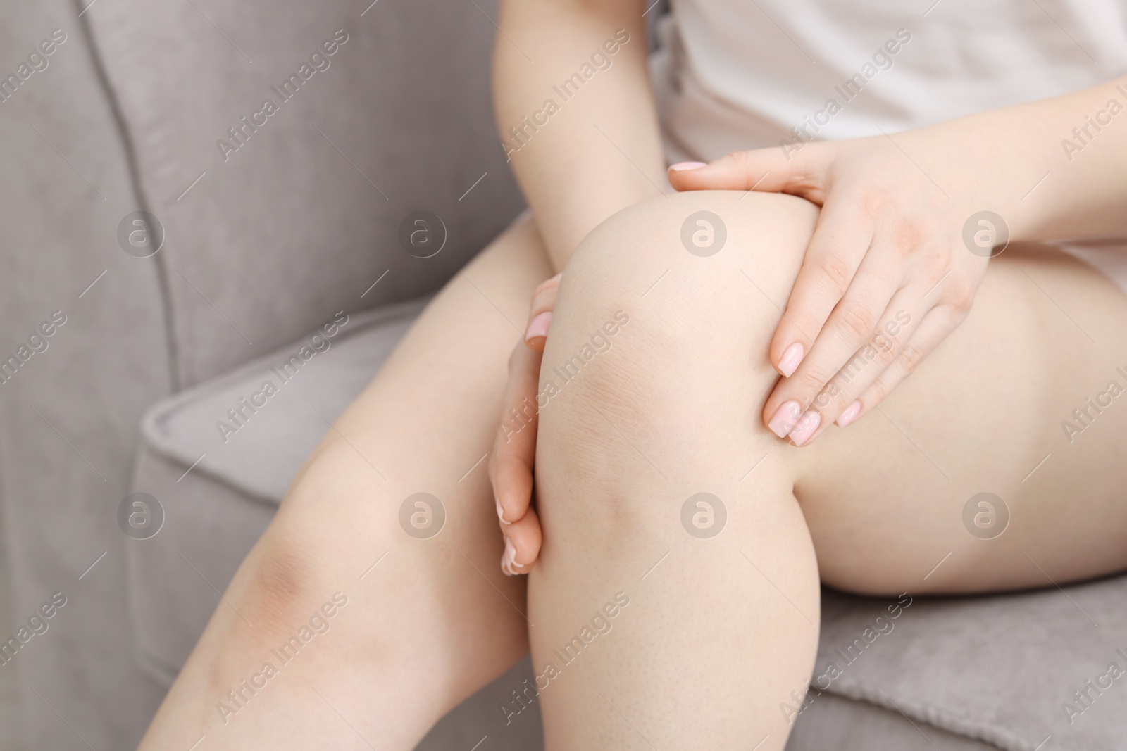 Photo of Young woman suffering from pain in knee on sofa at home, closeup