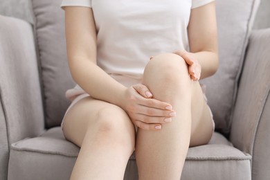 Photo of Young woman suffering from pain in knee on sofa at home, closeup