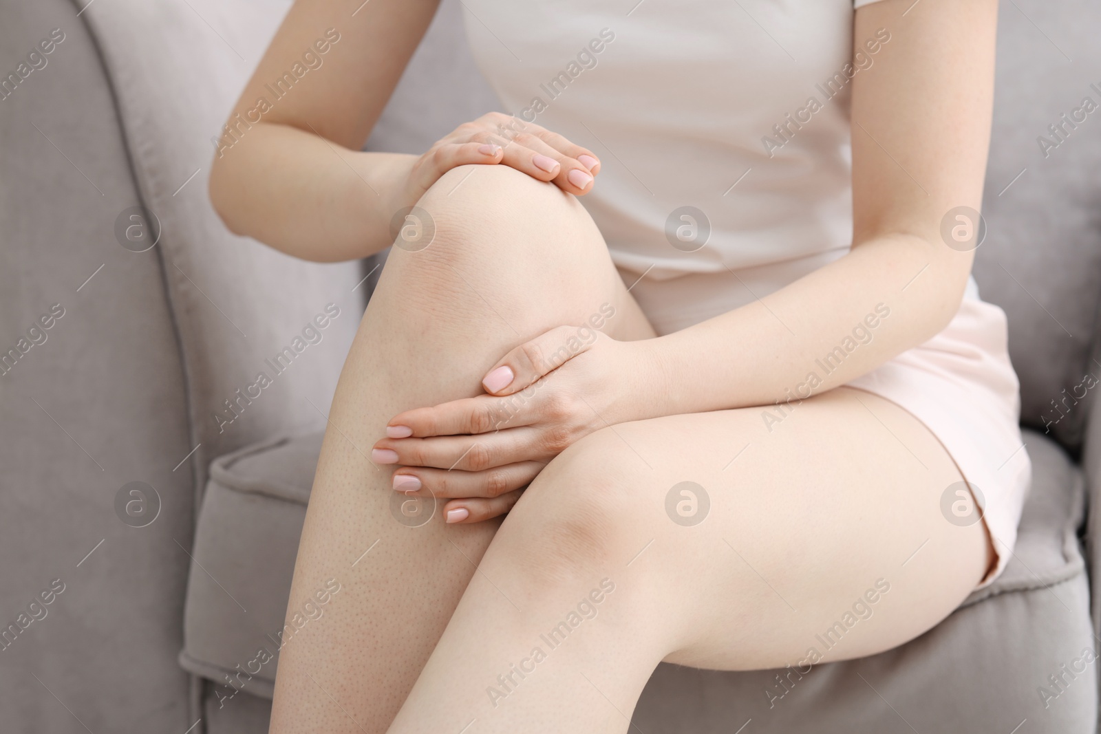 Photo of Young woman suffering from pain in knee on sofa at home, closeup