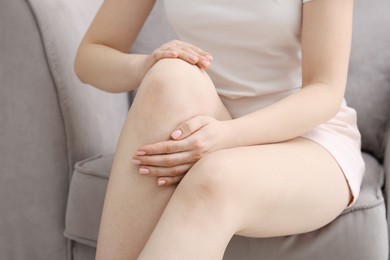 Photo of Young woman suffering from pain in knee on sofa at home, closeup