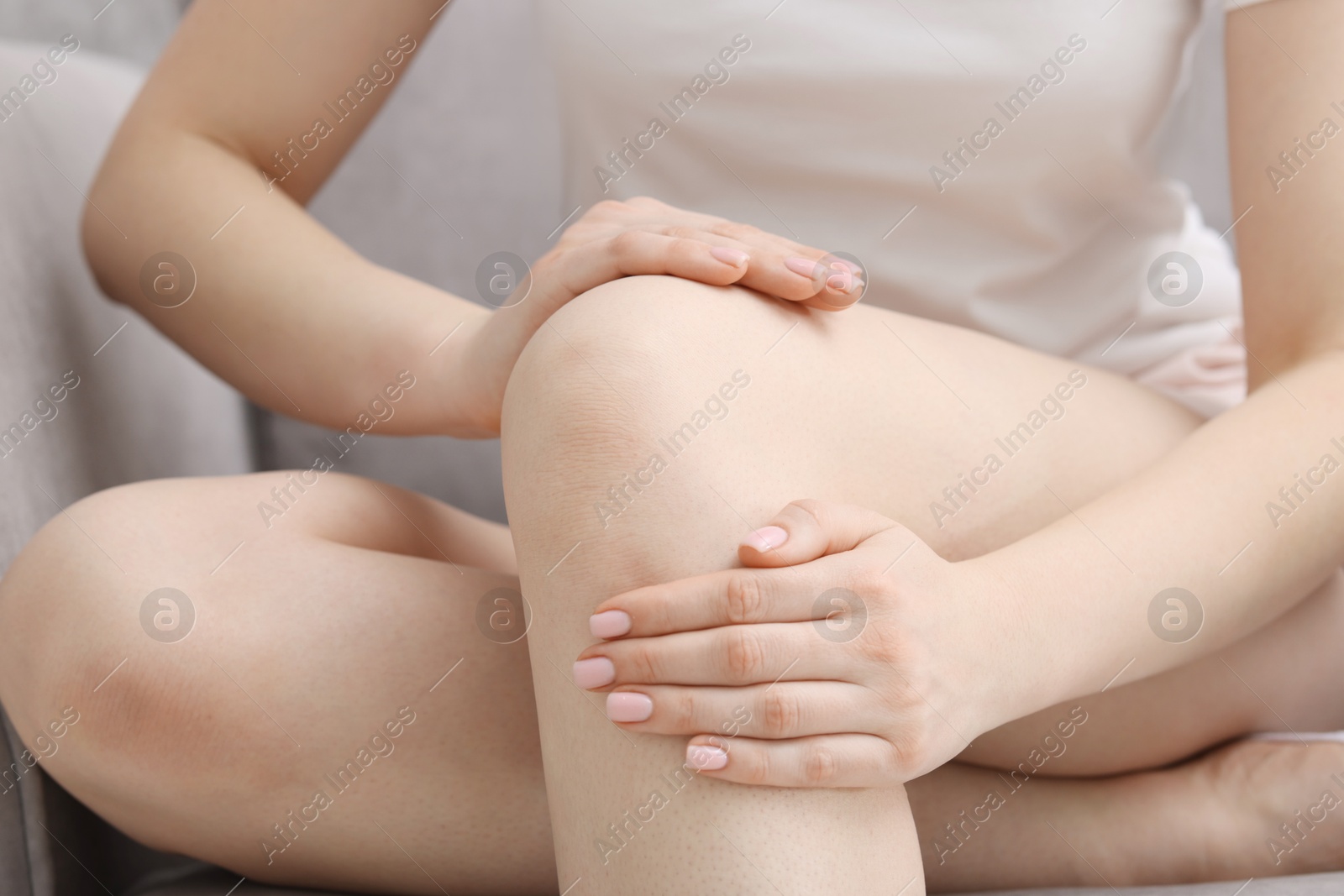 Photo of Young woman suffering from pain in knee on sofa at home, closeup