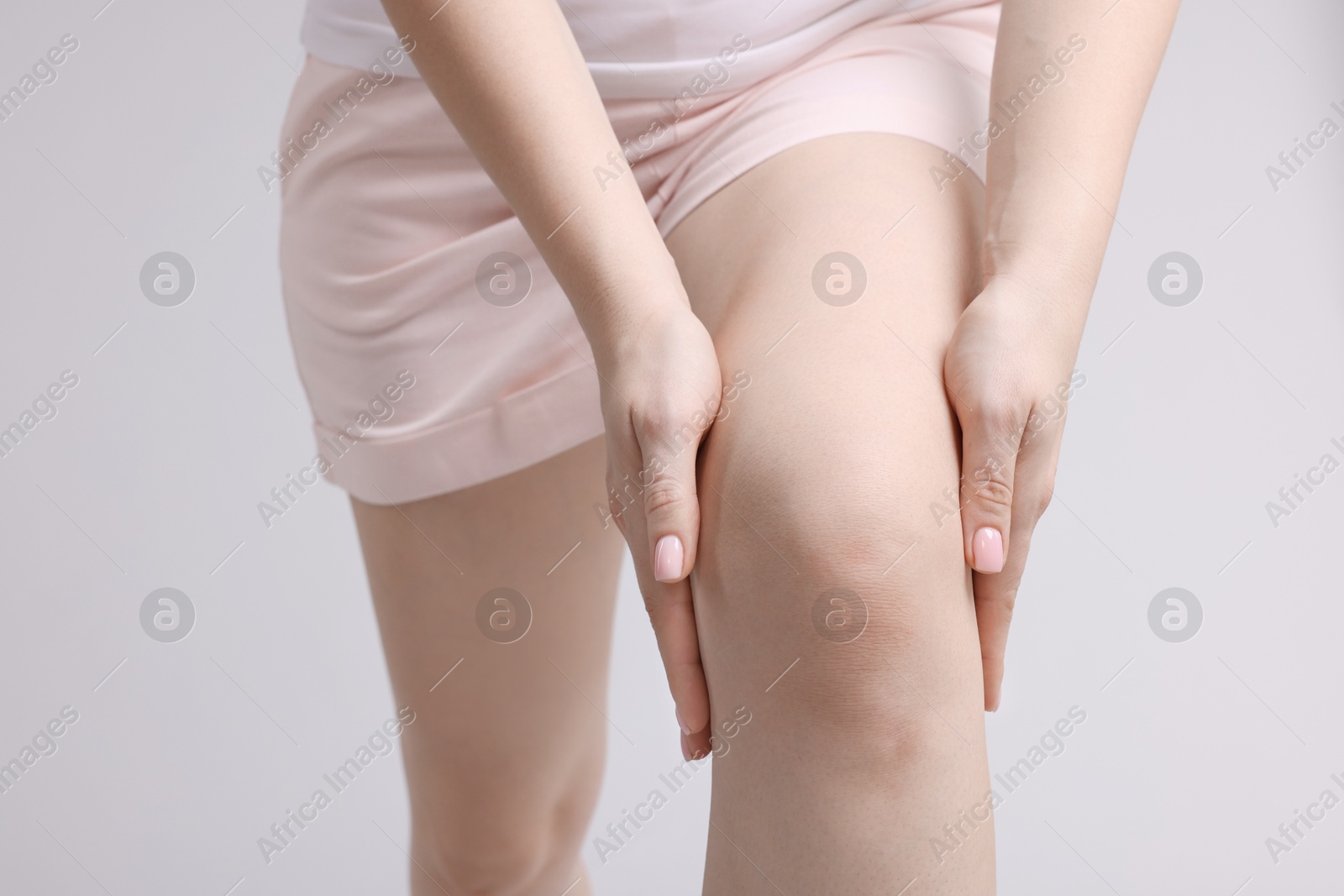 Photo of Young woman suffering from pain in knee on light grey background, closeup