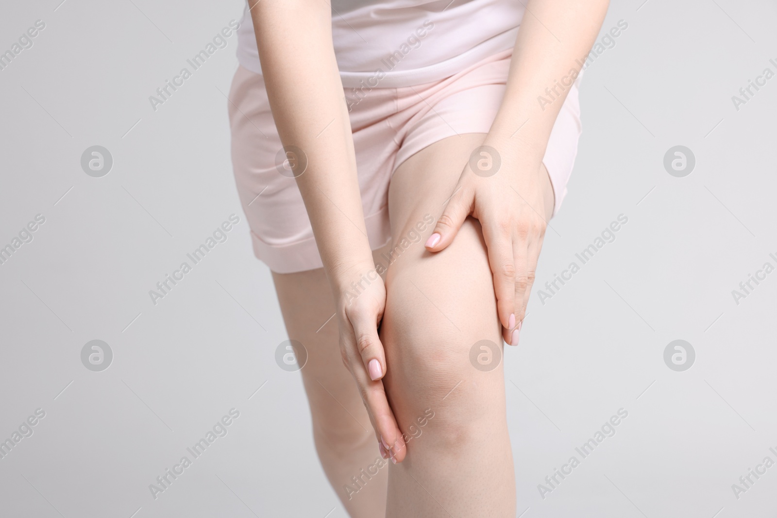 Photo of Young woman suffering from pain in knee on light grey background, closeup