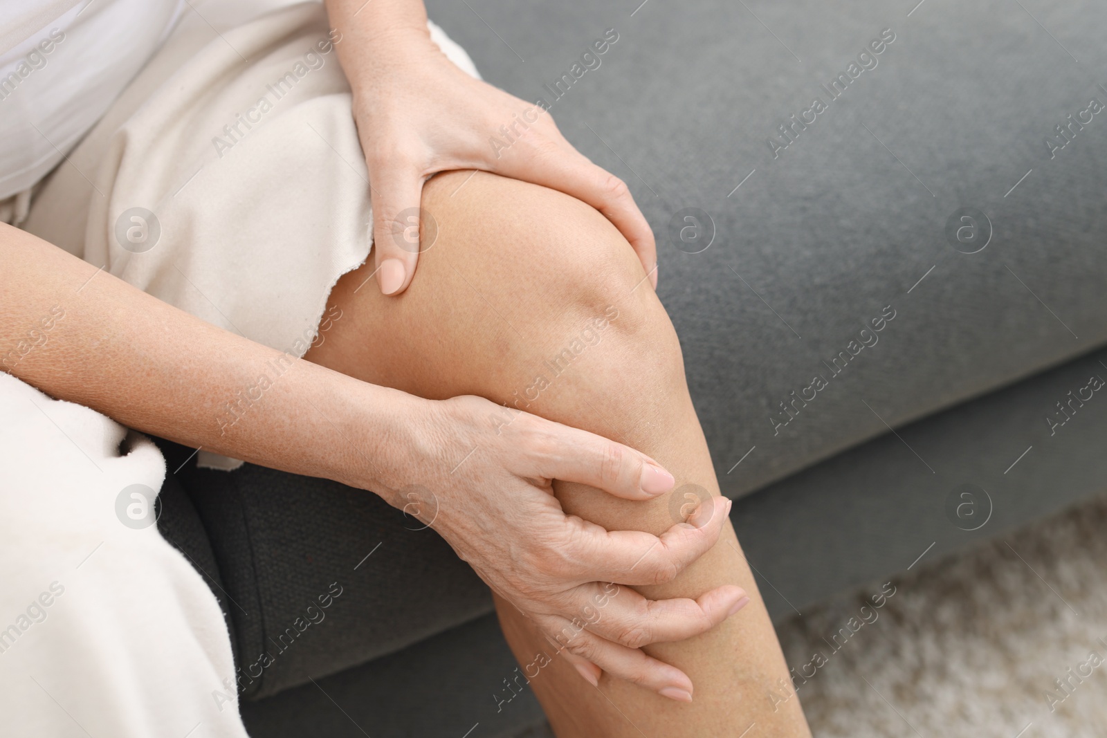 Photo of Woman suffering from pain in her knee on sofa, closeup