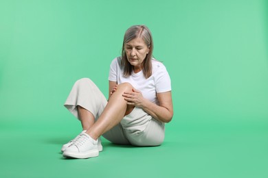 Photo of Senior woman suffering from knee pain on green background