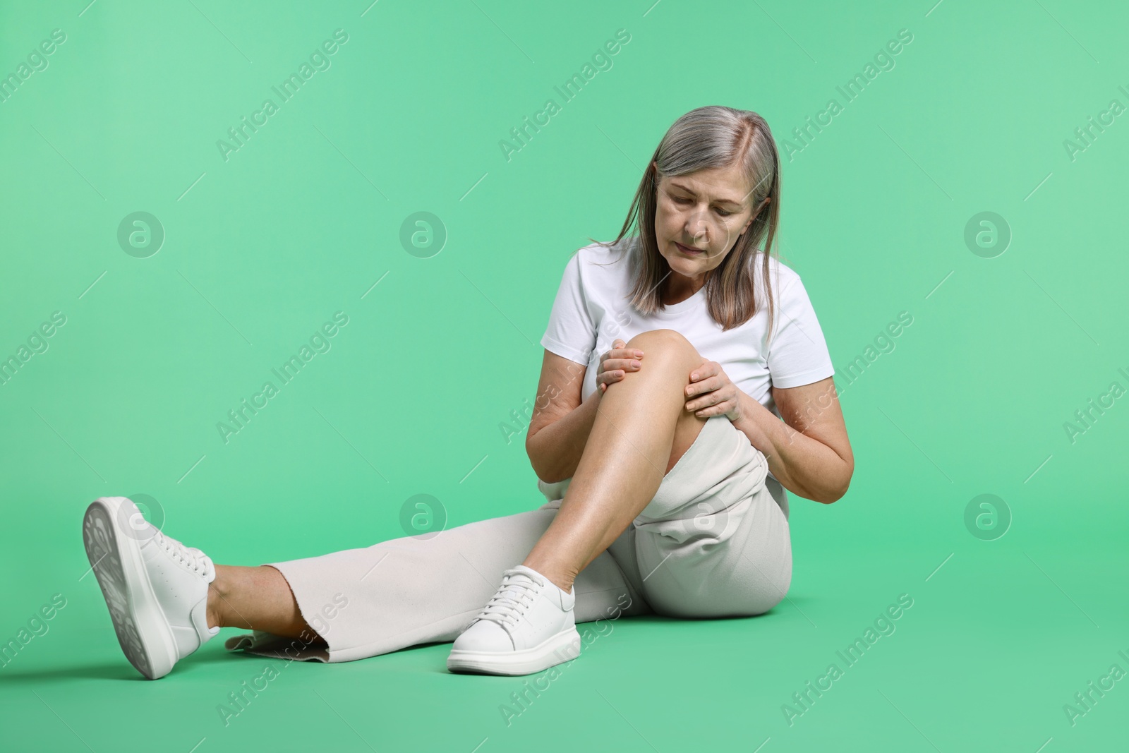 Photo of Senior woman suffering from knee pain on green background