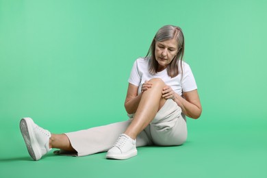 Photo of Senior woman suffering from knee pain on green background