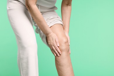 Photo of Woman suffering from pain in her knee on green background, closeup. Space for text