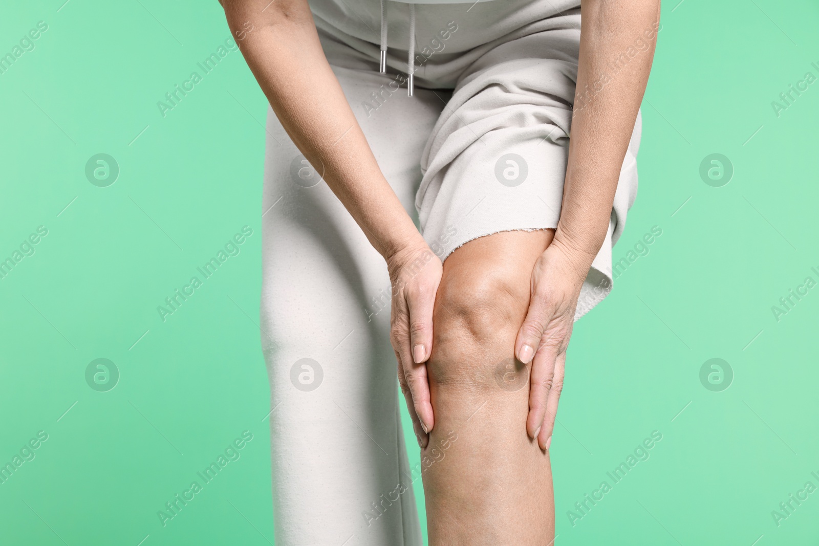 Photo of Woman suffering from pain in her knee on green background, closeup