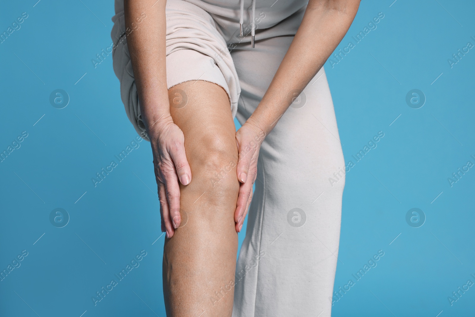 Photo of Woman suffering from pain in her knee on light blue background, closeup