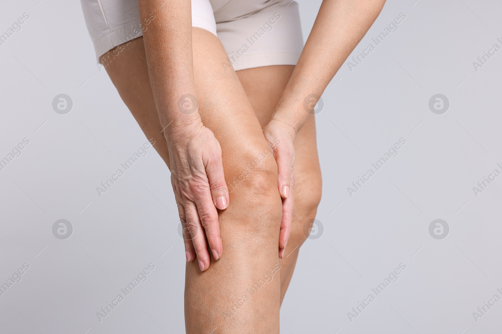 Photo of Woman suffering from pain in her knee on light grey background, closeup