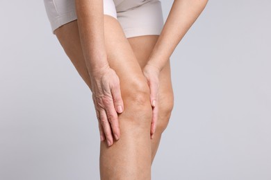 Photo of Woman suffering from pain in her knee on light grey background, closeup