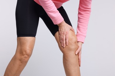 Photo of Woman suffering from pain in her knee on light grey background, closeup