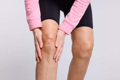 Photo of Woman suffering from pain in her knee on light grey background, closeup