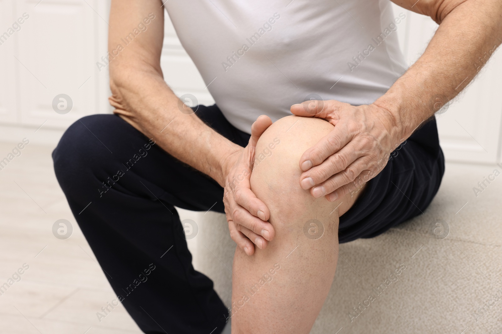 Photo of Senior man suffering from knee pain on pouf indoors, closeup