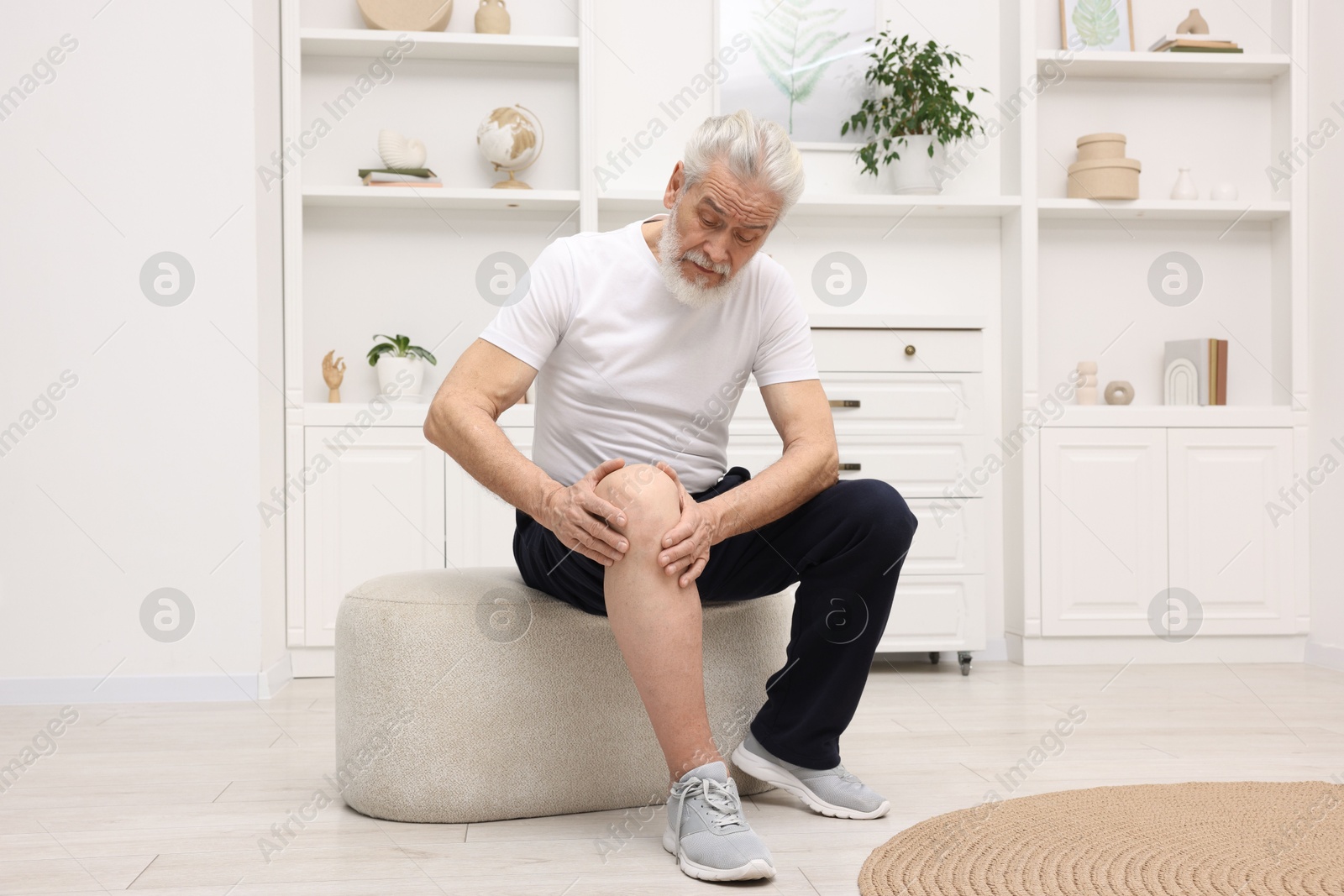 Photo of Senior man suffering from knee pain on pouf at home