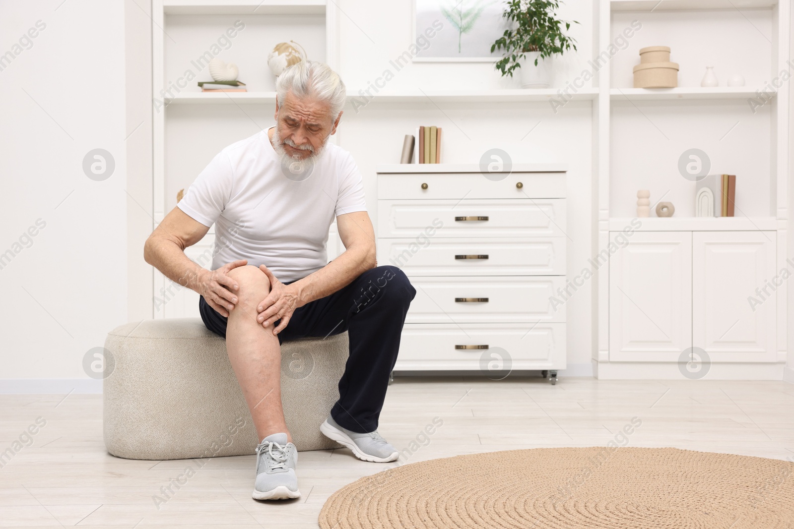 Photo of Senior man suffering from knee pain on pouf at home