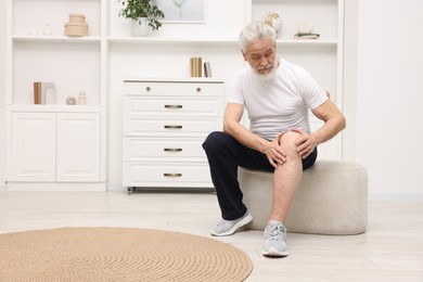 Photo of Senior man suffering from knee pain on pouf at home