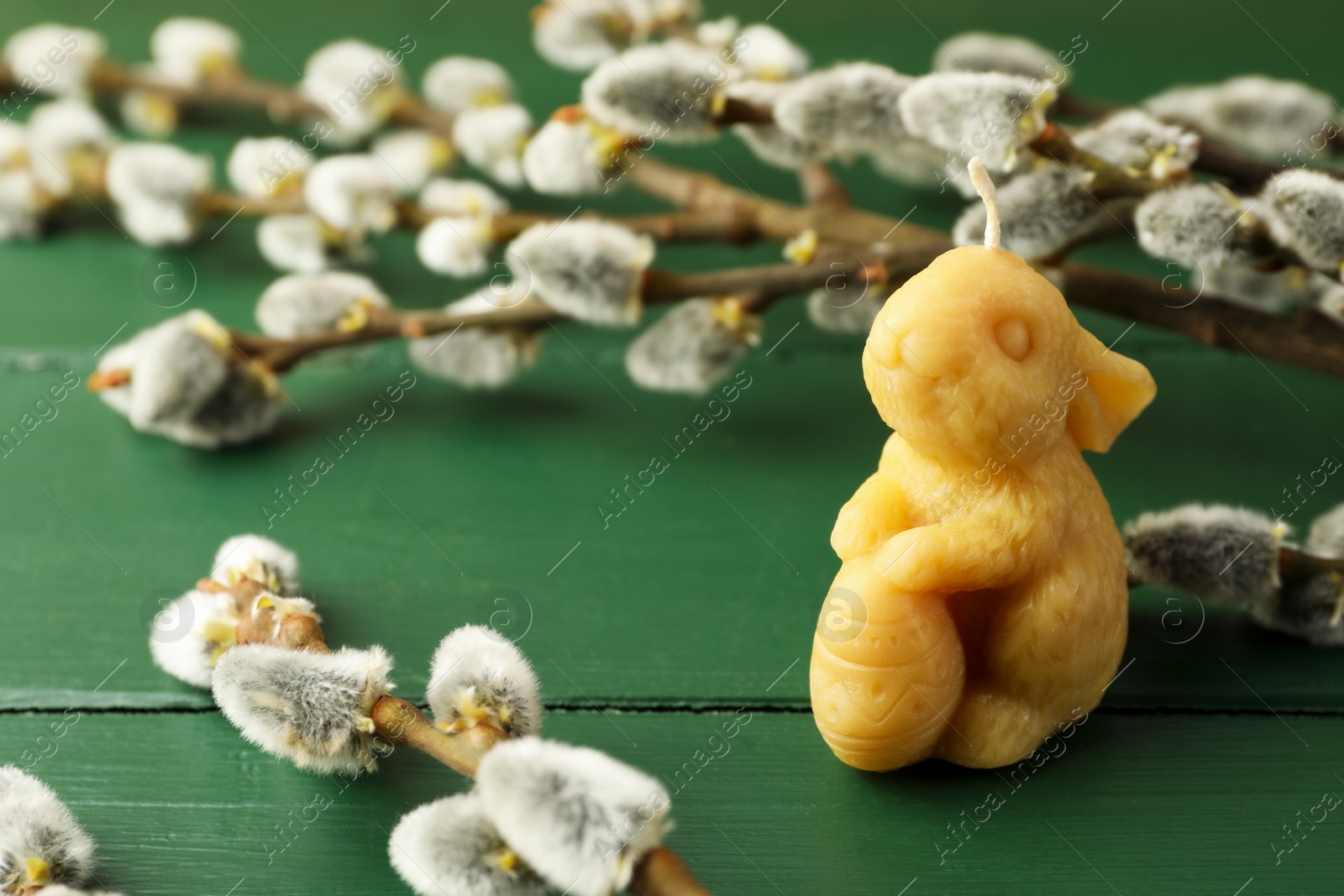 Yellow bunny-shaped candle and willow branches on green wooden table, closeup. Easter decor Photo of Yellow bunny-shaped candle and willow branches on green wooden table, closeup. Easter decor