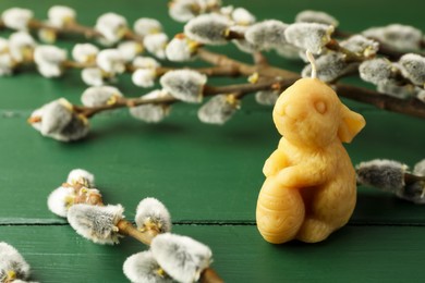 Photo of Yellow bunny-shaped candle and willow branches on green wooden table, closeup. Easter decor