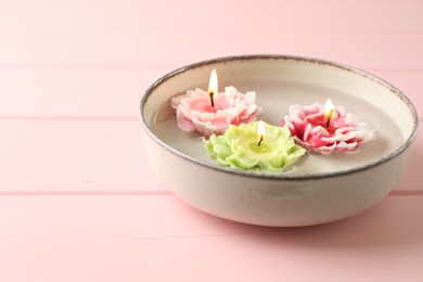 Photo of Beautiful burning flower shaped candles in dish with water on pink wooden table, closeup. Space for text