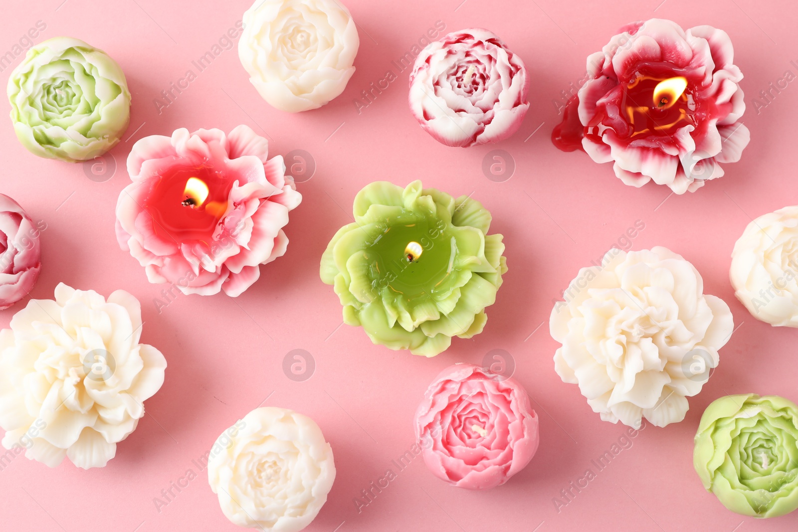 Photo of Beautiful burning flower shaped candles on pink background, flat lay