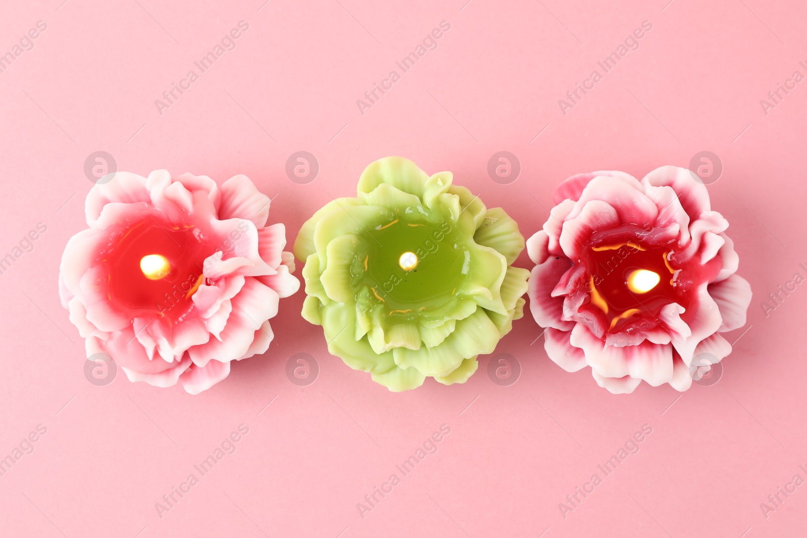 Photo of Beautiful burning flower shaped candles on pink background, flat lay