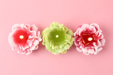 Photo of Beautiful burning flower shaped candles on pink background, flat lay