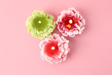 Photo of Beautiful burning flower shaped candles on pink background, flat lay