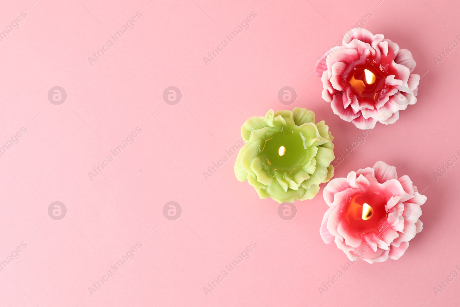 Photo of Beautiful burning flower shaped candles on pink background, flat lay. Space for text