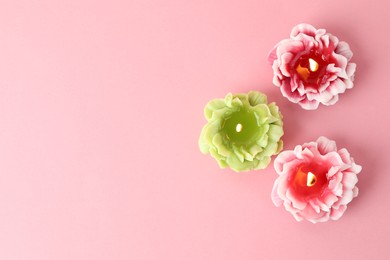 Photo of Beautiful burning flower shaped candles on pink background, flat lay. Space for text