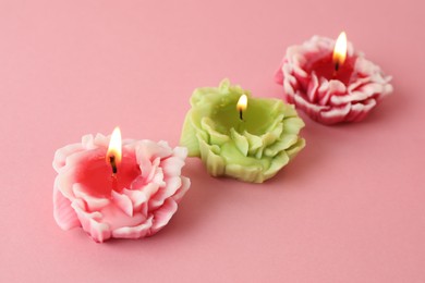 Photo of Beautiful burning flower shaped candles on pink background, closeup