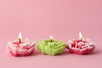 Photo of Beautiful burning flower shaped candles on pink background, closeup. Space for text