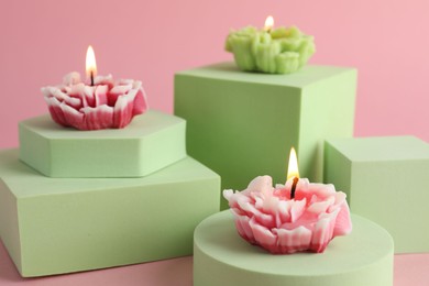 Photo of Beautiful burning flower shaped candles on pink background, closeup