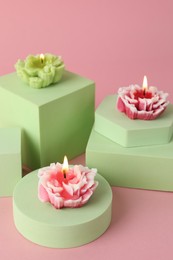 Photo of Beautiful burning flower shaped candles on pink background, closeup