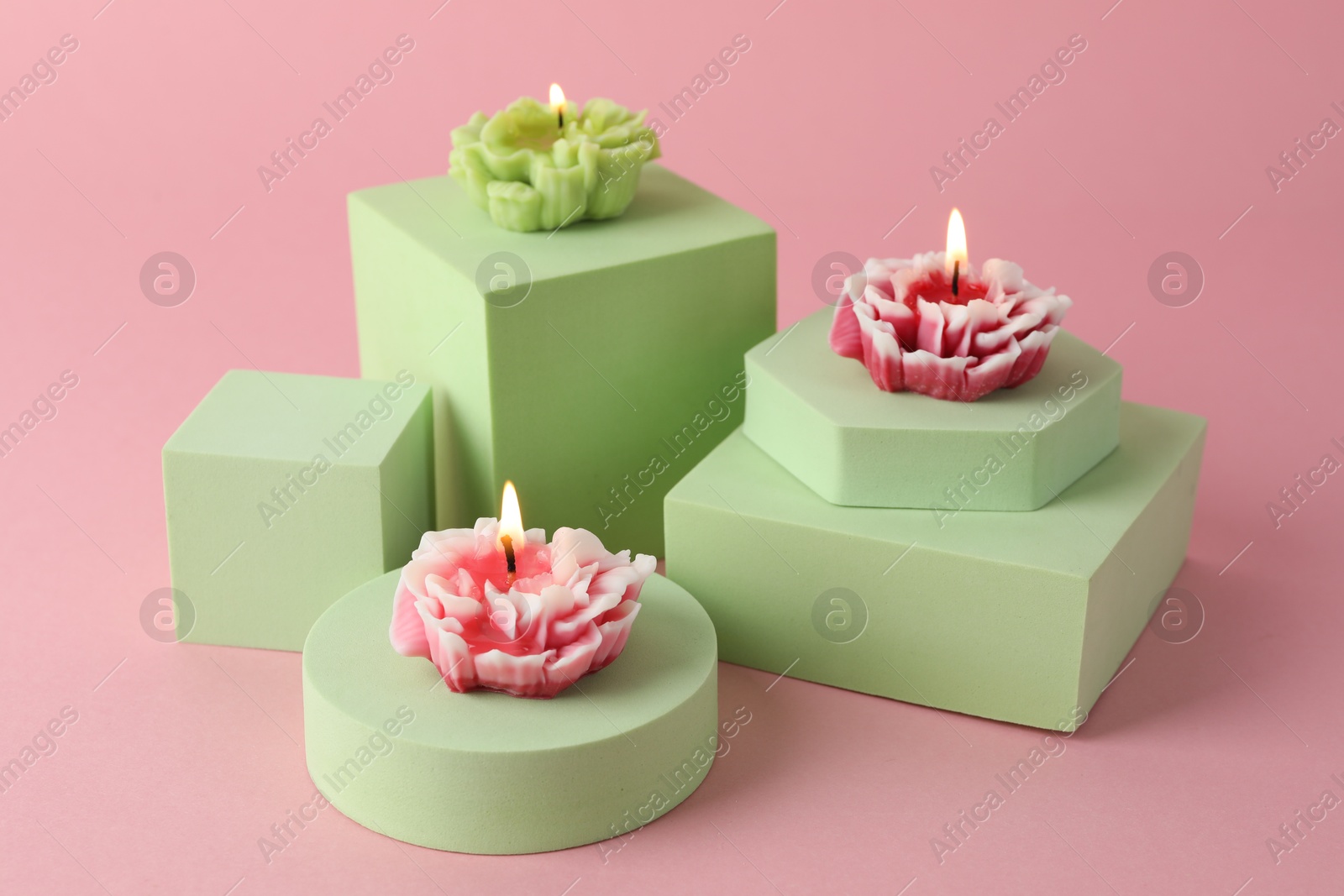 Photo of Beautiful burning flower shaped candles on pink background, closeup