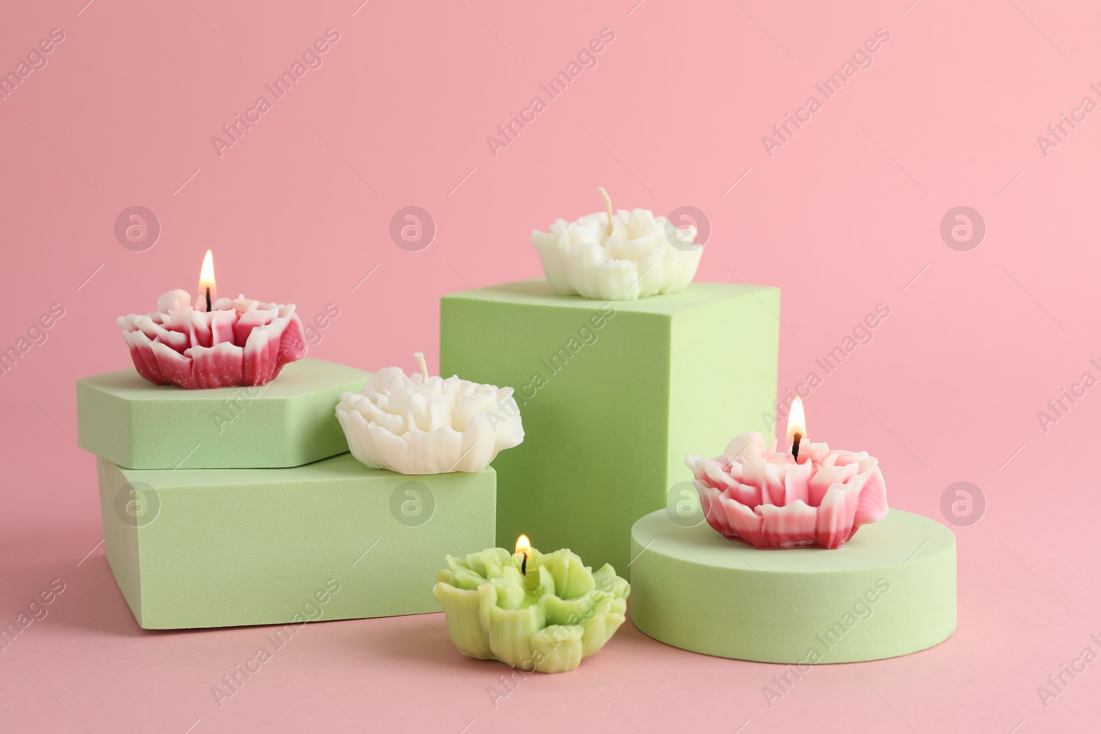 Photo of Beautiful burning flower shaped candles on pink background