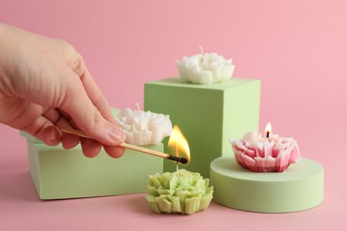 Photo of Woman lighting up beautiful flower shaped candles on pink background, closeup