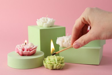 Photo of Woman lighting up beautiful flower shaped candles on pink background, closeup