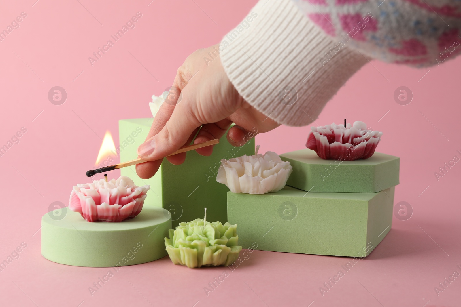 Photo of Woman lighting up beautiful flower shaped candles on pink background, closeup