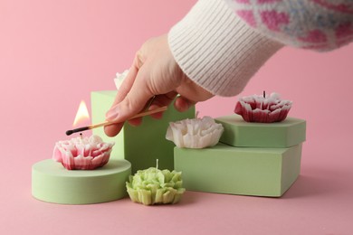 Photo of Woman lighting up beautiful flower shaped candles on pink background, closeup