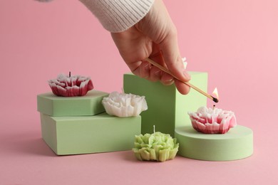 Photo of Woman lighting up beautiful flower shaped candles on pink background, closeup