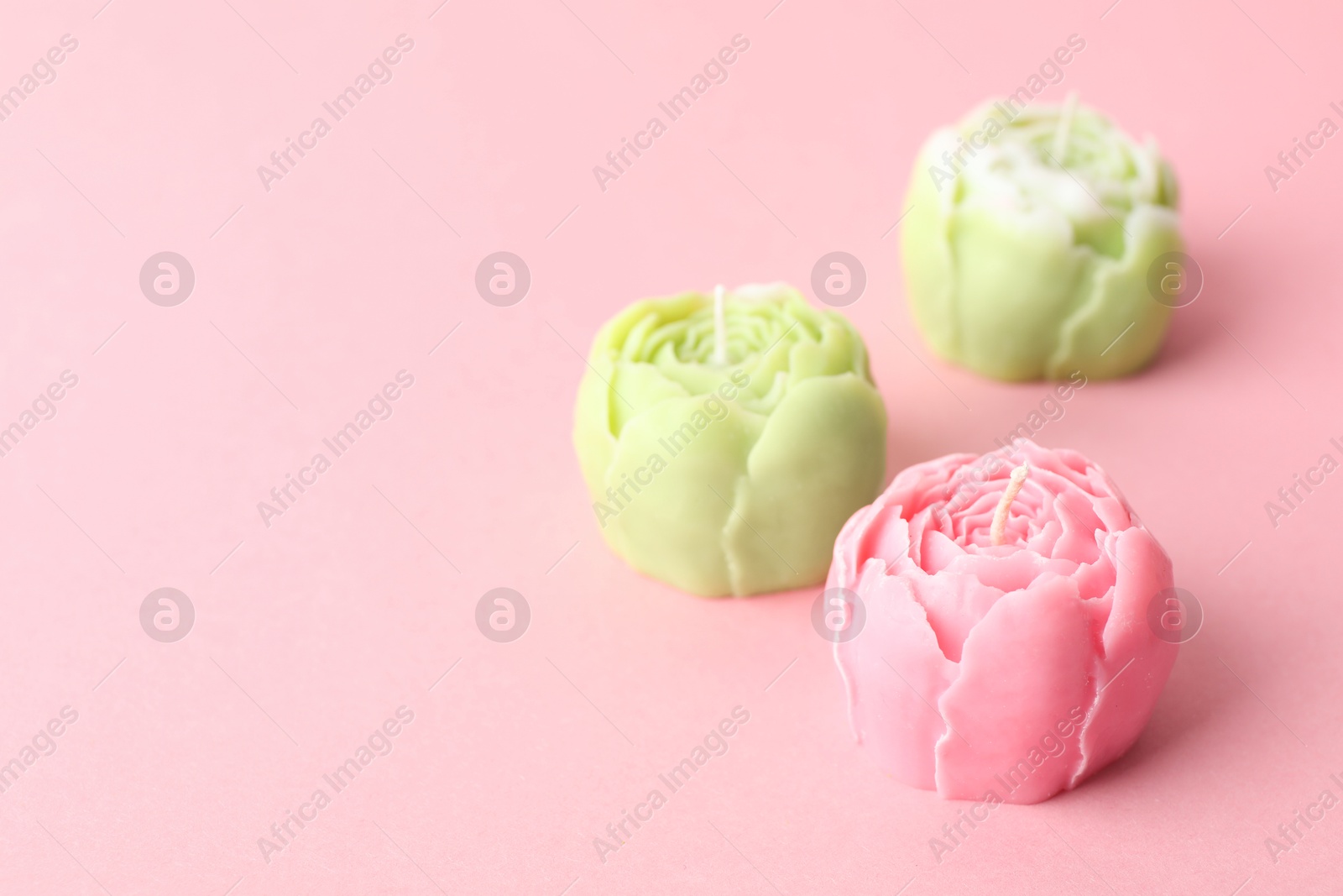 Photo of Beautiful flower shaped candles on pink background, closeup. Space for text