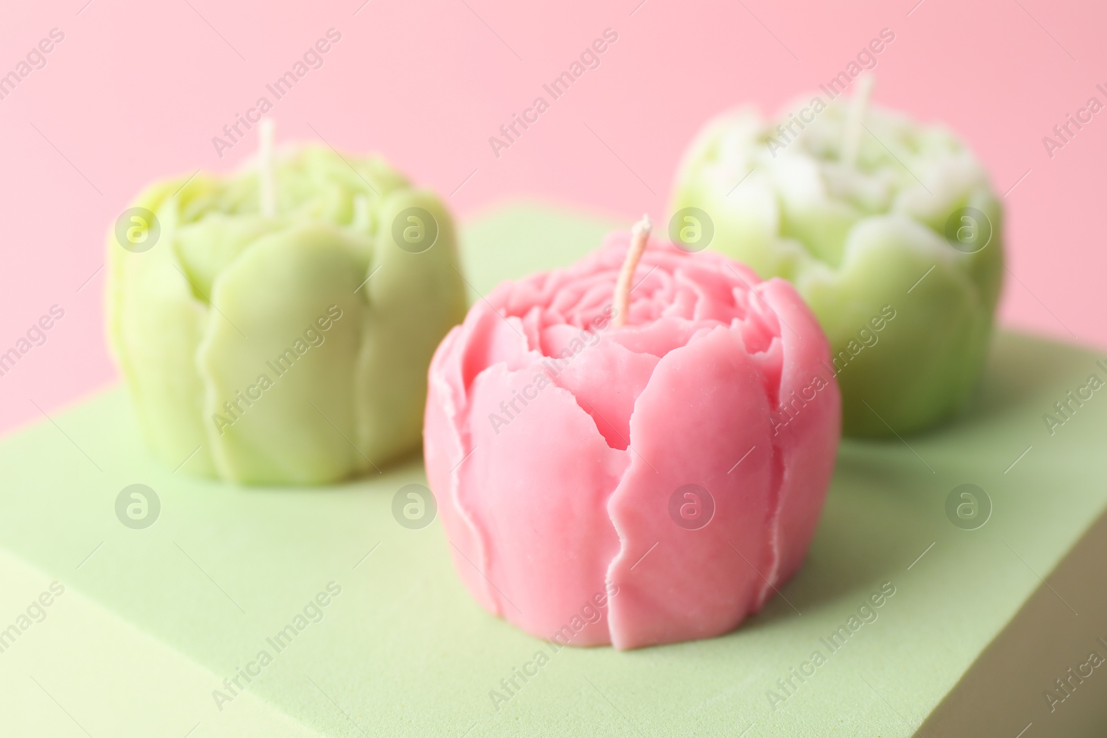 Photo of Beautiful flower shaped candles on pink background, closeup