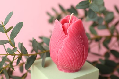 Photo of Beautiful flower shaped candle and leaves on pink background, closeup