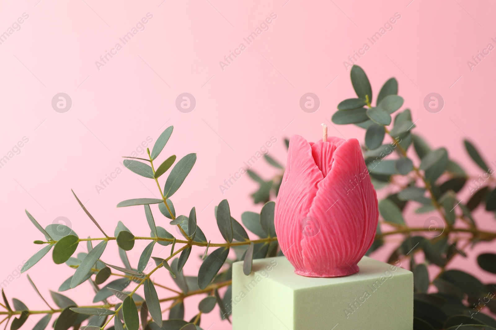 Photo of Beautiful flower shaped candle and leaves on pink background, closeup. Space for text